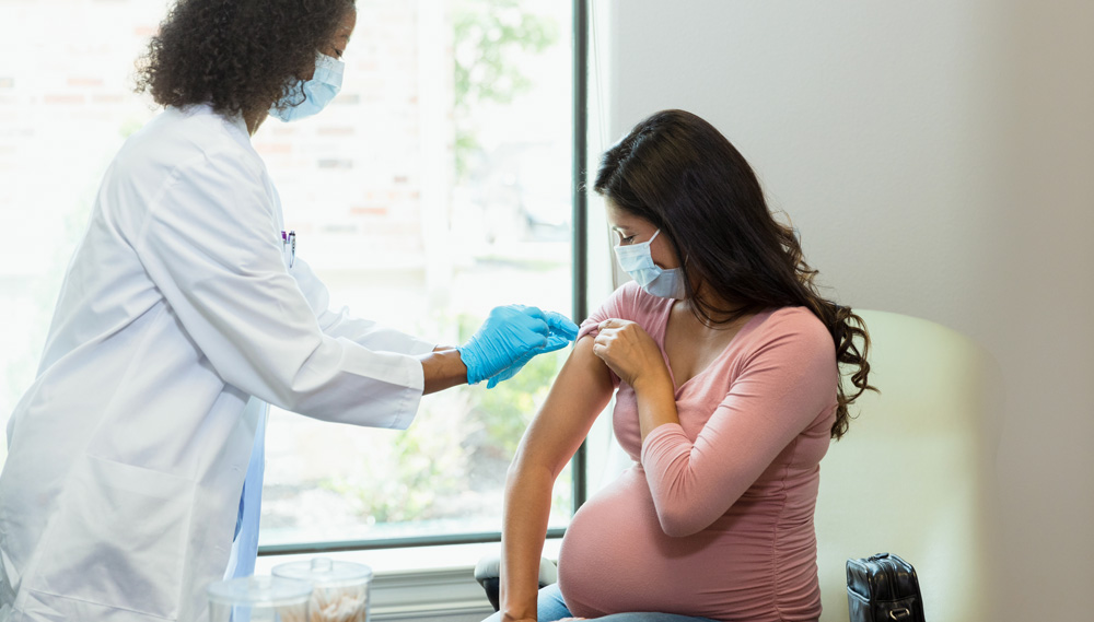 A doctor places a band-aid on a pregnant woman's shoulder after vaccination.