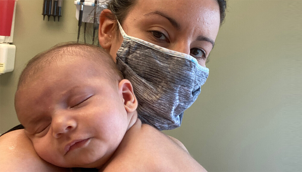 Christina holding her baby. Christina is wearing a mask.