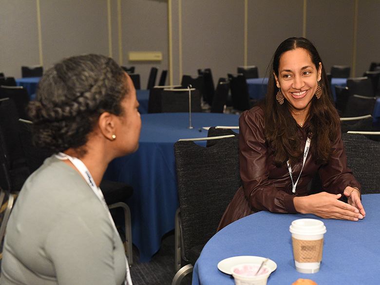 Two conference attendees sitting together at a table engaged in conversation.