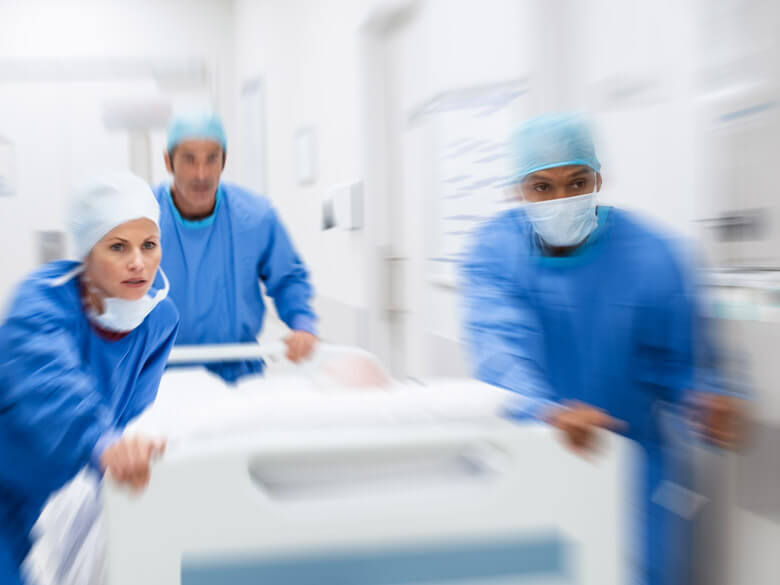 three medical professionals in blue scrubs urgently pushing a gurney 