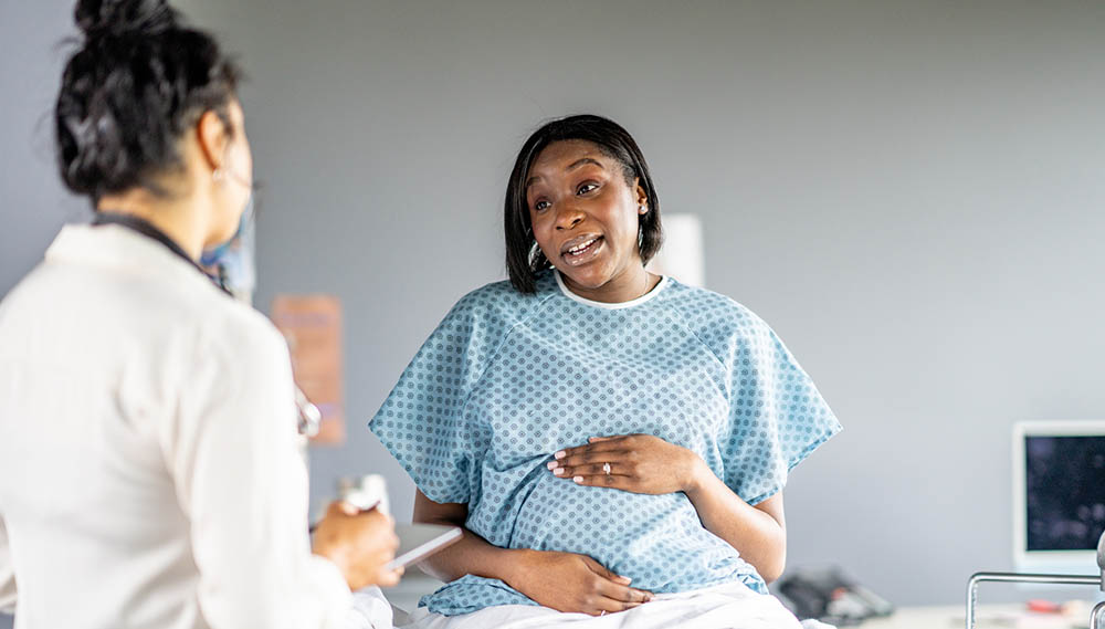 A pregnant woman holds her belly while talking to her doctor.