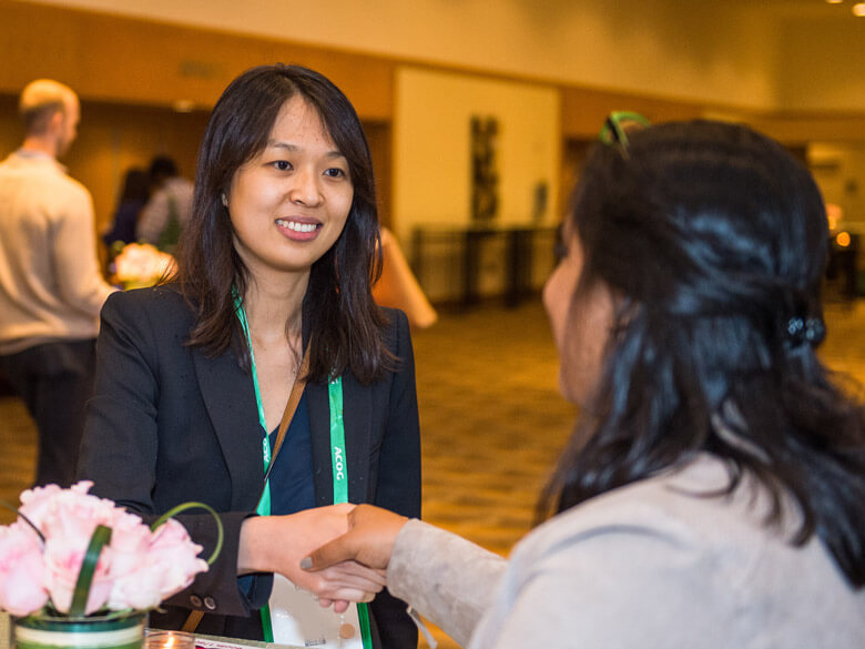 two members chatting next to a bouquet of pink roses