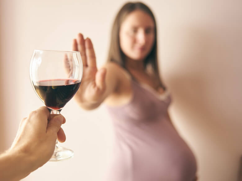Pregnant woman declining a glass of red wine.