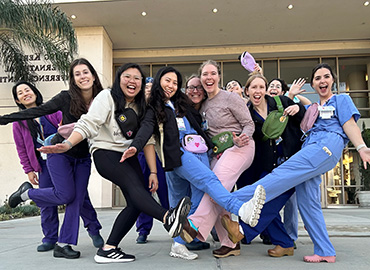 A smiling group of medical students in scrubs pose outside a medical center