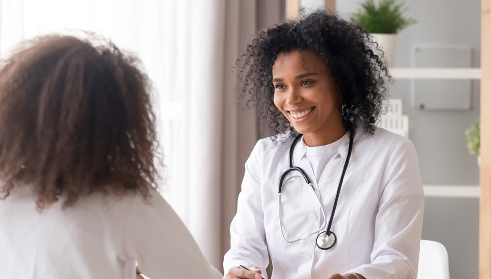 A doctor sits across from a patient, smiling and talking.