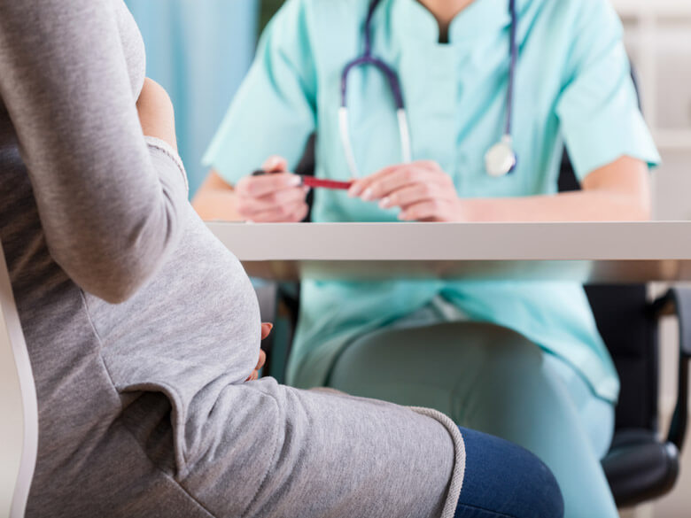 Pregnant woman sitting across from a person in blue scrubs with stethoscope.