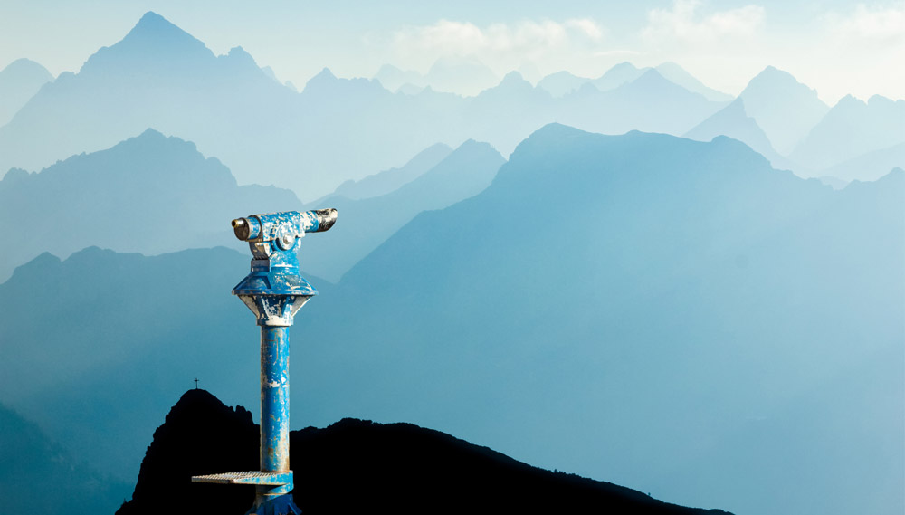 A telescope mounted on a hill with a view of mountains for a great distance. 