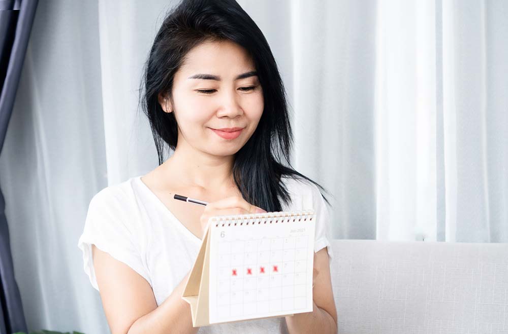 Young woman marks red x's on a calendar to show when she has her period.